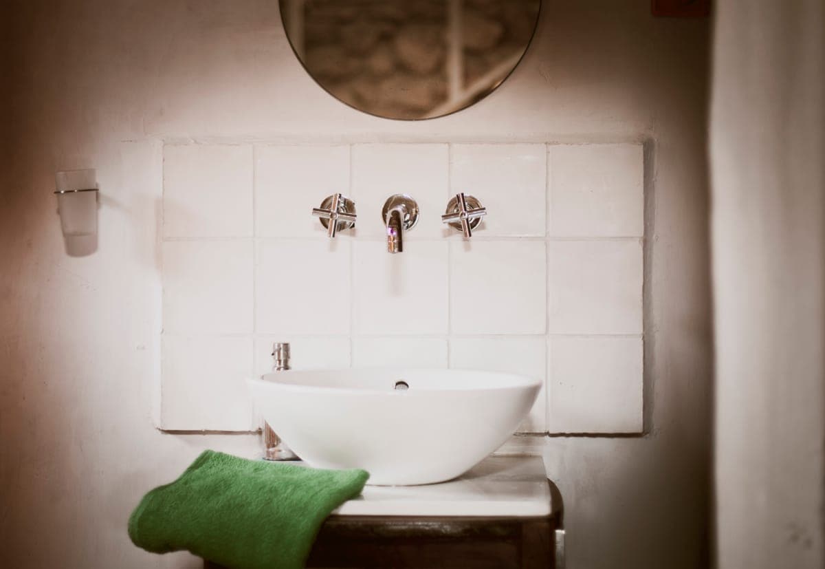 Detalle del lavabo blanco con espejo redondo y azulejo tradicional