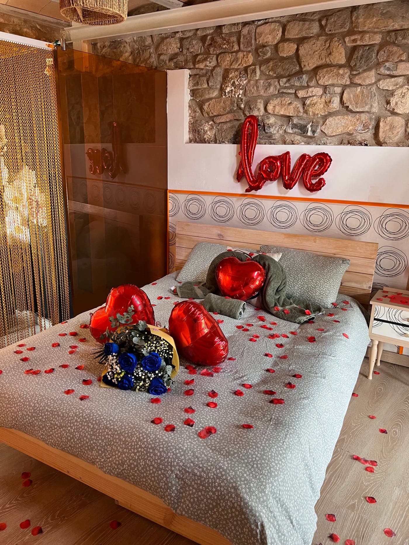 Vista general del dormitorio con el montaje del pack preparado: globos, ramo y pétalos sobre la cama