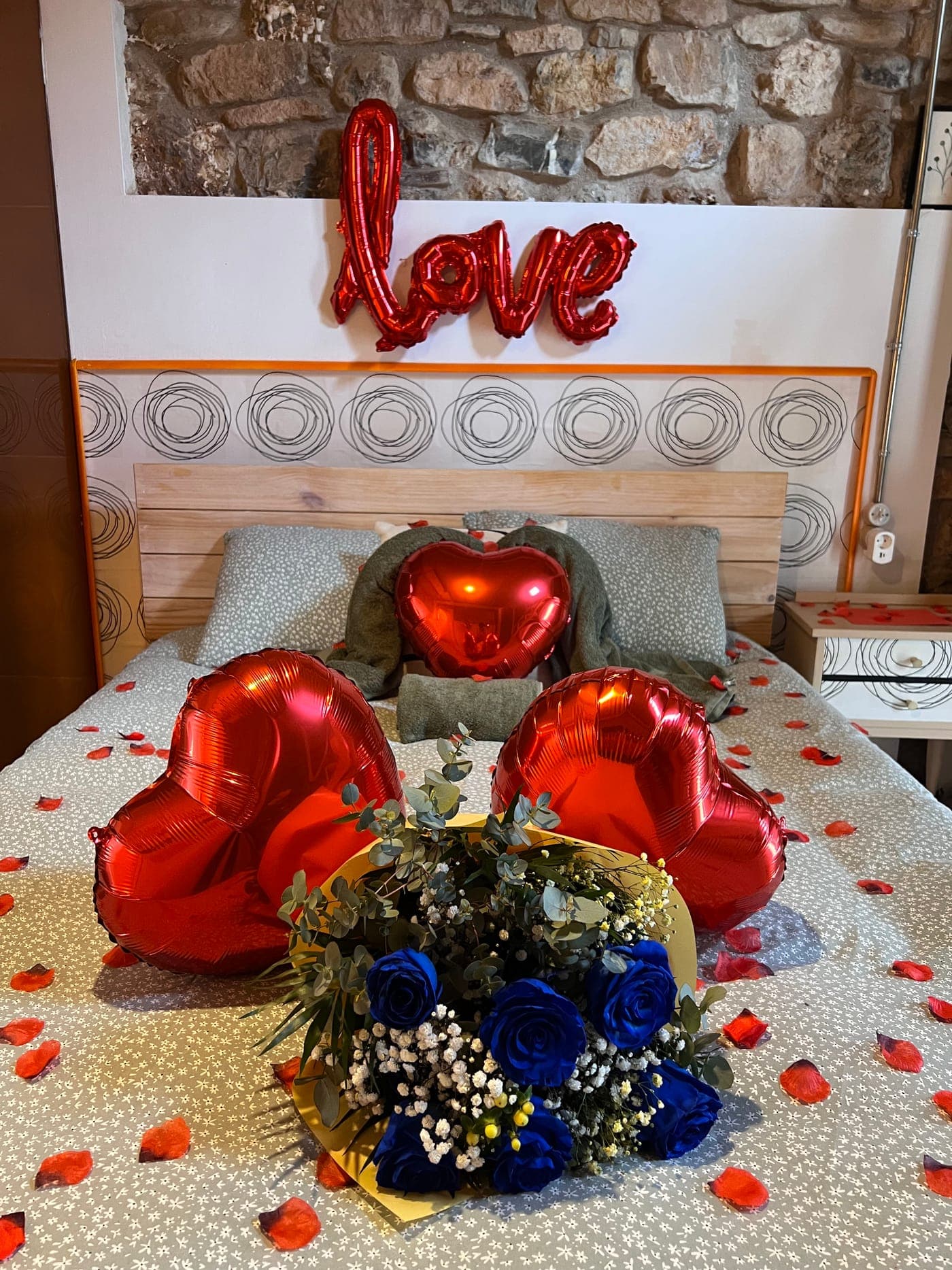 El montaje del pack sobre la cama: globos con forma de corazón, globo de letras, ramo de rosas azules y pétalos repartidos