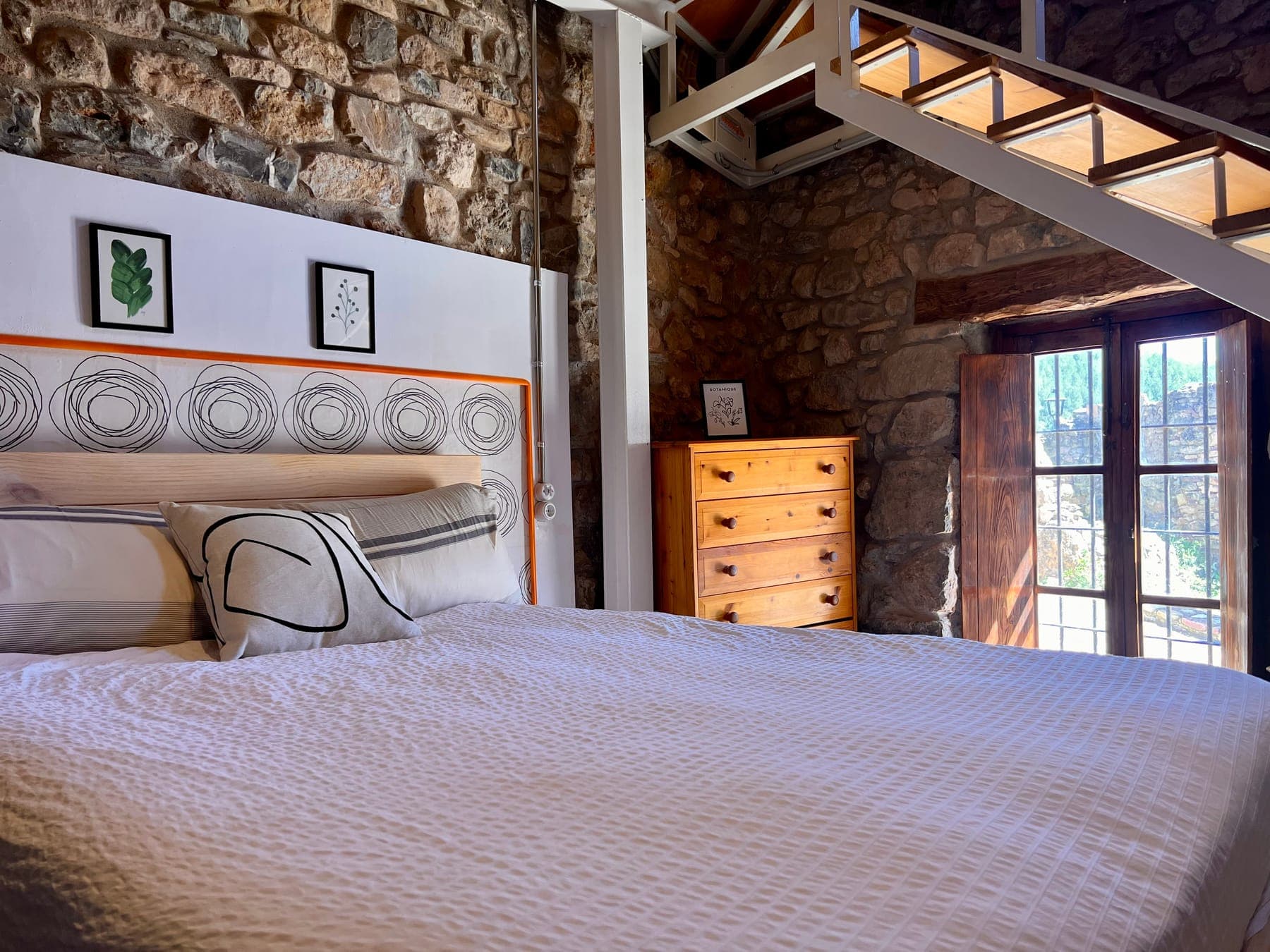 Dormitorio con cama doble, pared de piedra y cómoda de madera