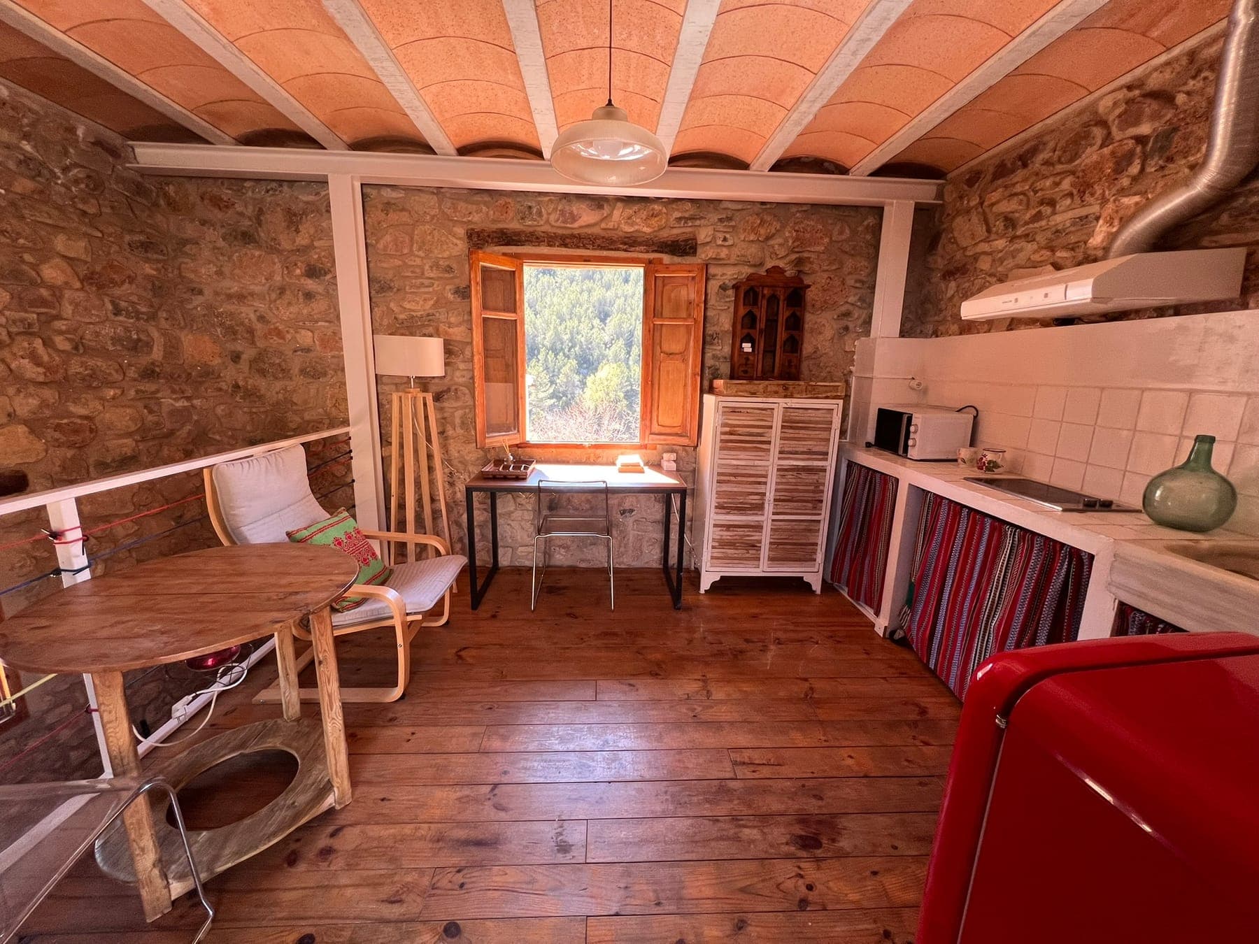 Vista general de la sala de estar con el techo de bovedilla, la ventana al bosque y la cocina