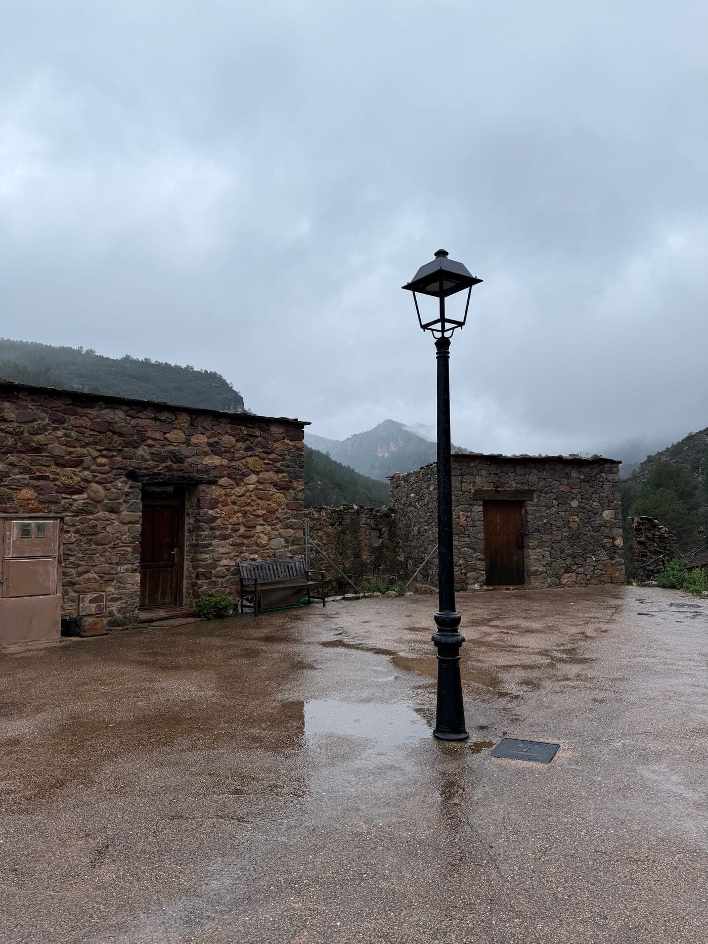 La plaza empedrada del pueblo un día de lluvia, con la farola de forja
