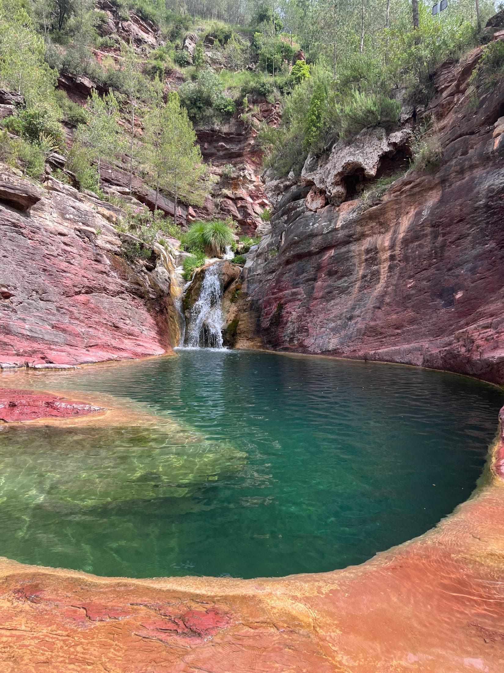 El Pozo Negro: a turquoise natural pool over red rock with a small waterfall, in Fuentes de Ayódar